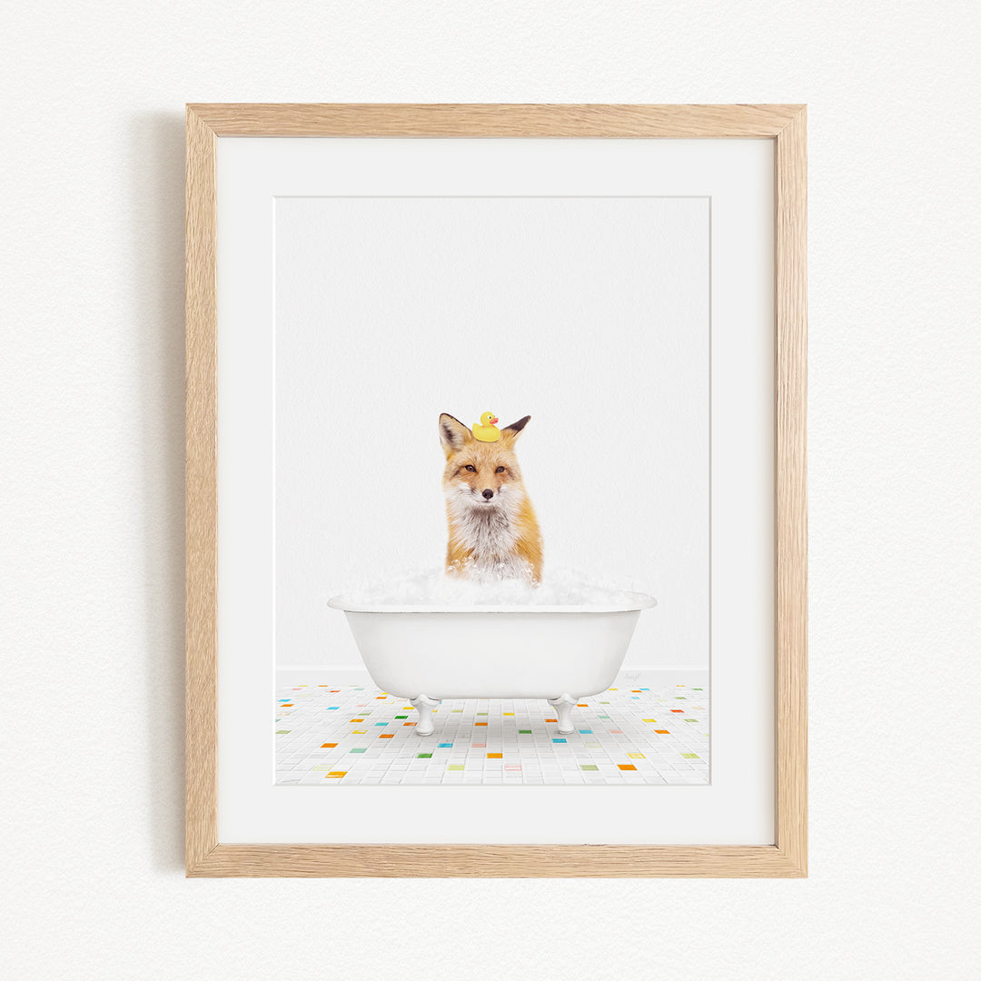 A framed image of a fox sitting in a white bathtub filled with bubbles, with a yellow rubber duck floating on the water.