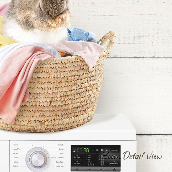A cat is sitting in a woven laundry basket filled with clothes, placed next to a washing machine.