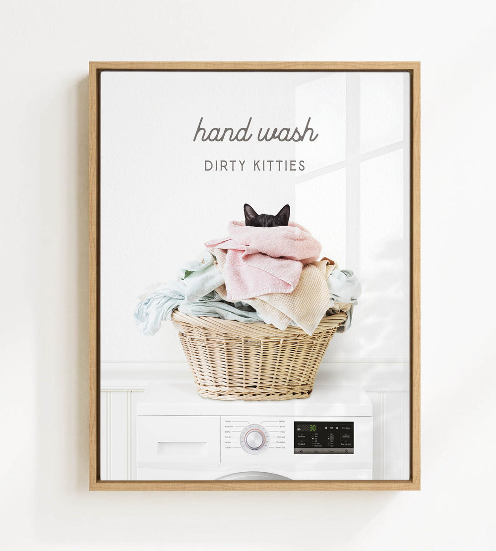 A framed image depicting a cat sitting in a basket filled with laundry, with the text "hand wash dirty kitties" above the basket.
