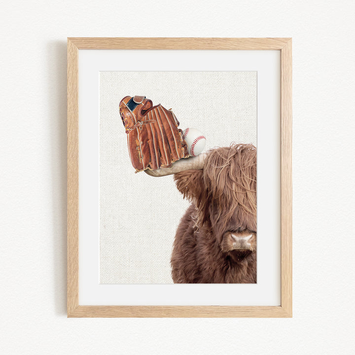 A framed image depicting a cow with a baseball glove on its head.