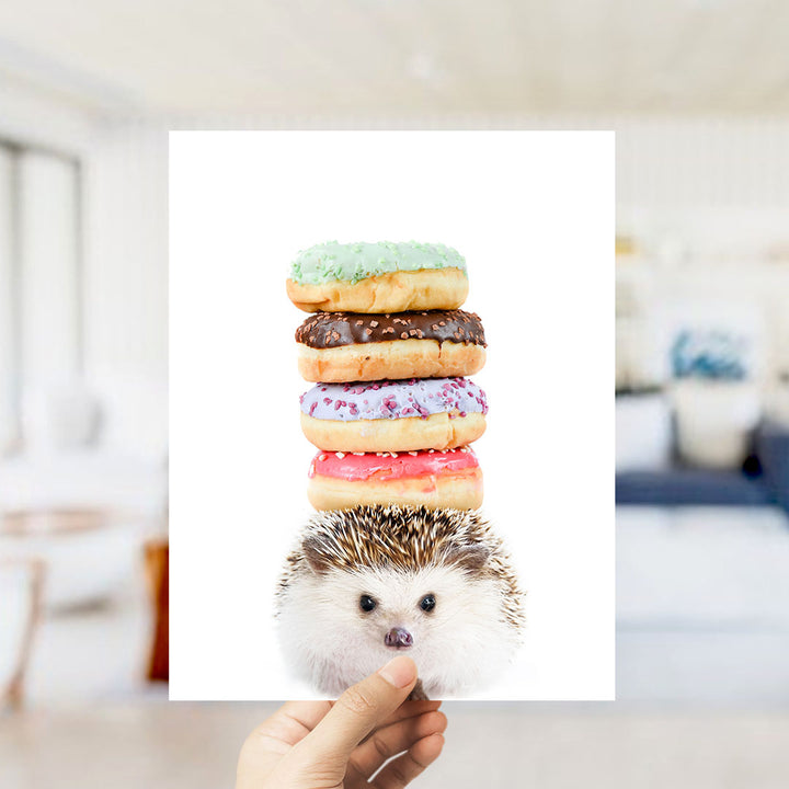 A hand holds up a hedgehog with a stack of colorful donuts on its head, creating a playful and whimsical scene.