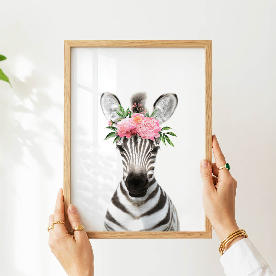 A person's hands are holding a framed picture of a zebra with a floral crown on its head.