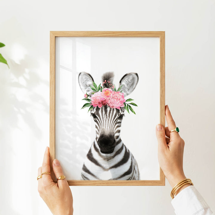 A person's hands are holding a framed picture of a zebra with a floral crown on its head.