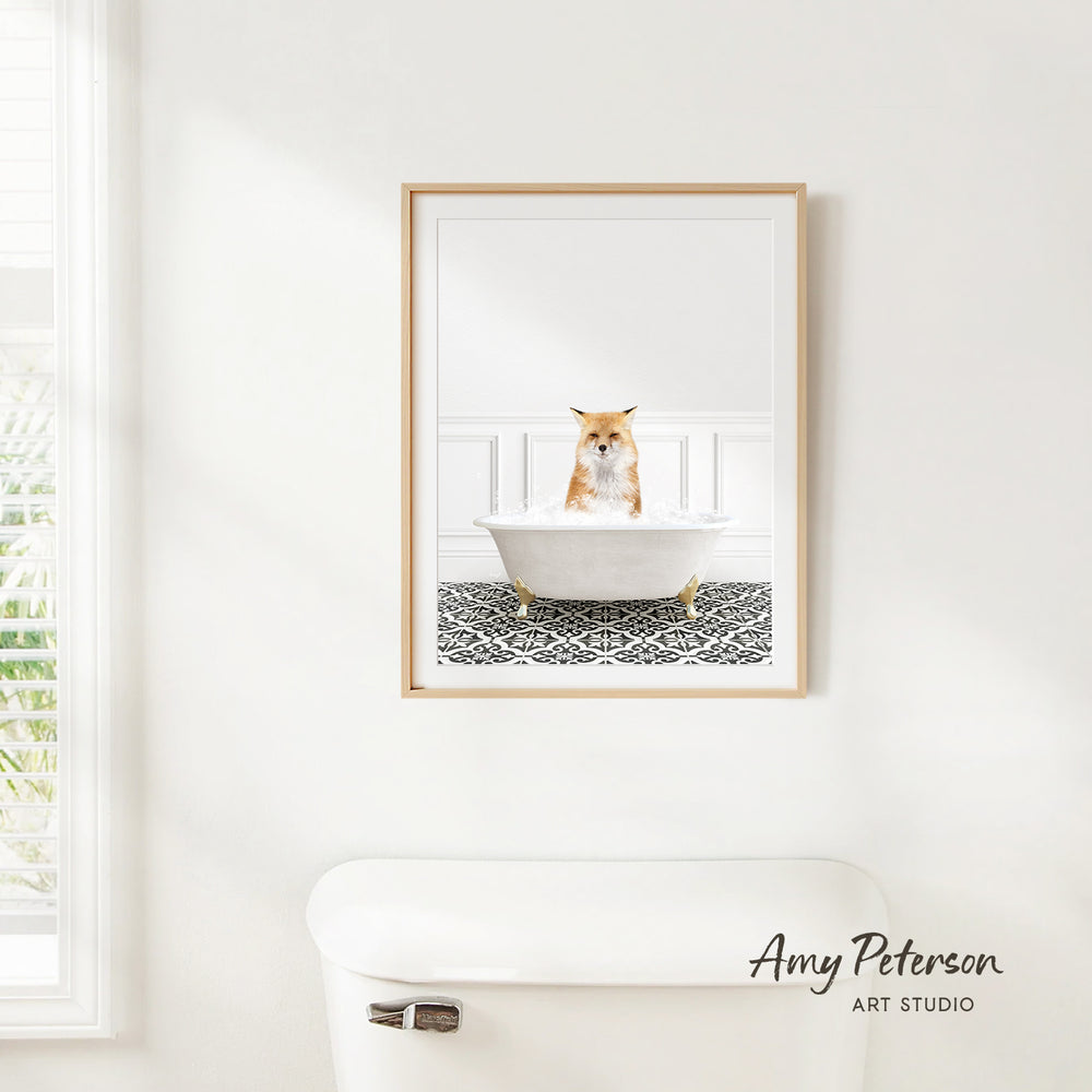 A framed image of a cat sitting in a bathtub, with a patterned tile floor beneath it, is hanging on a white wall in a bathroom.
