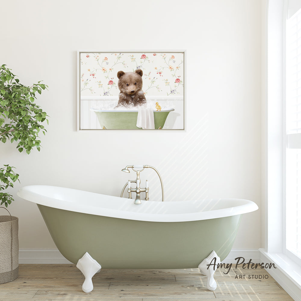 A framed image of a bear sitting in a bathtub is displayed on the wall above a green clawfoot bathtub in a bathroom.