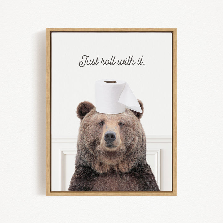 A framed image of a brown bear wearing a roll of toilet paper on its head, with the text "Just roll with it."