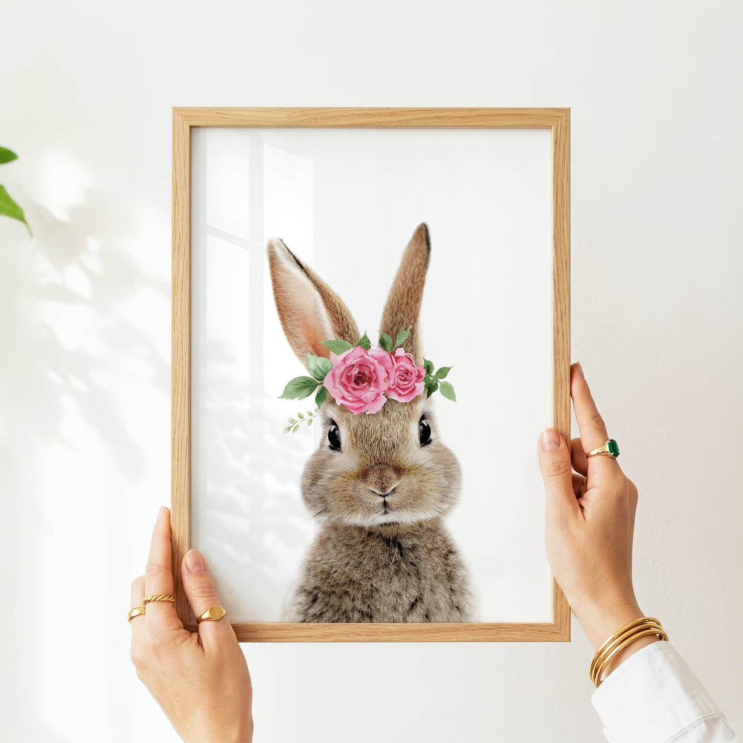 A person's hands are holding a picture frame with a picture of a rabbit inside it, which has a flower crown on its head.