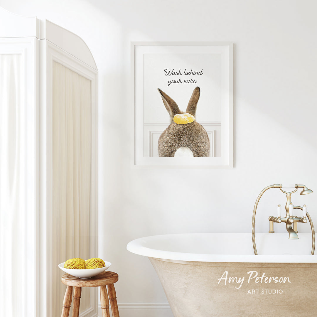 a bathroom with a framed poster of a rabbit on the wall, a wooden stool with a bowl of fruit, and a claw-foot bathtub.