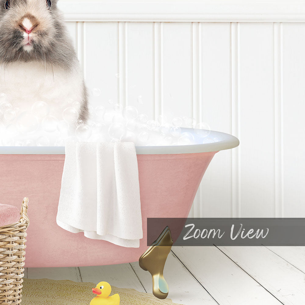 A fluffy gray and white rabbit sitting in a pink bathtub filled with bubbles, surrounded by a yellow rubber duck and a white basket.
