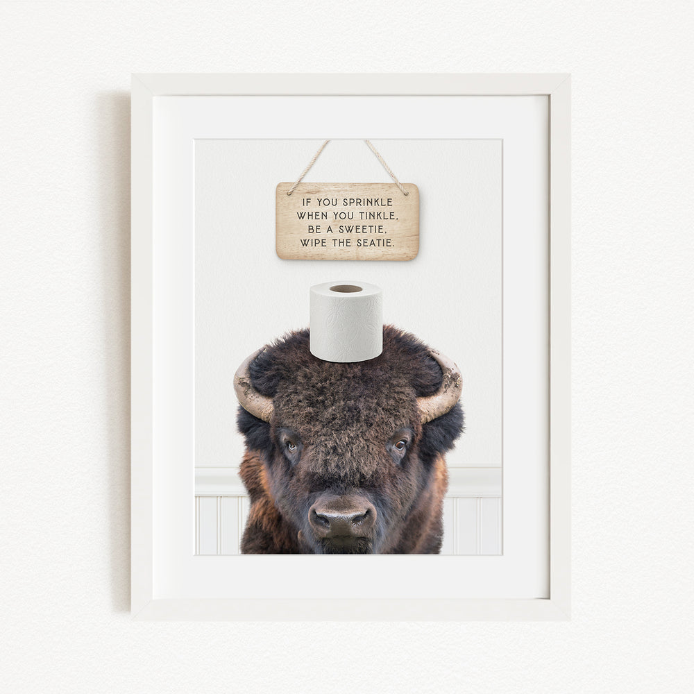 A framed image of a bison with a sign above it that reads "If you sprinkle when you twinkle, wipe the seagull".