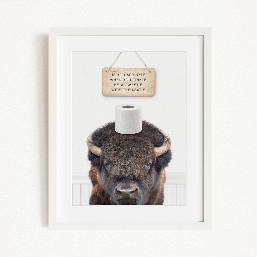 A framed image of a bison with a sign above it that reads "If you sprinkle when you twinkle, wipe the seagull".