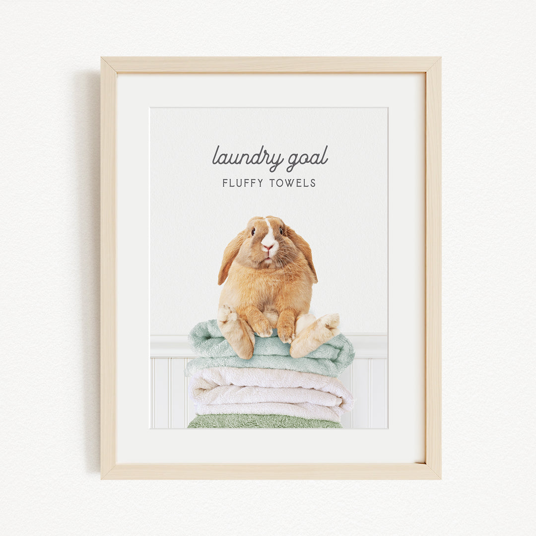 A framed image of a fluffy towel with a rabbit sitting on top of it, accompanied by the text "laundry goal FLUFFY TOWELS".