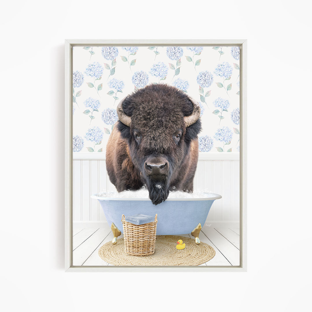 A buffalo is sitting in a blue bathtub filled with water, surrounded by a wicker basket and a yellow rubber duck.