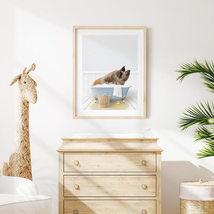 A framed image of a pig sitting in a bathtub, with a giraffe figurine next to it, is displayed on a wall in a room with a wooden dresser and a potted plant.