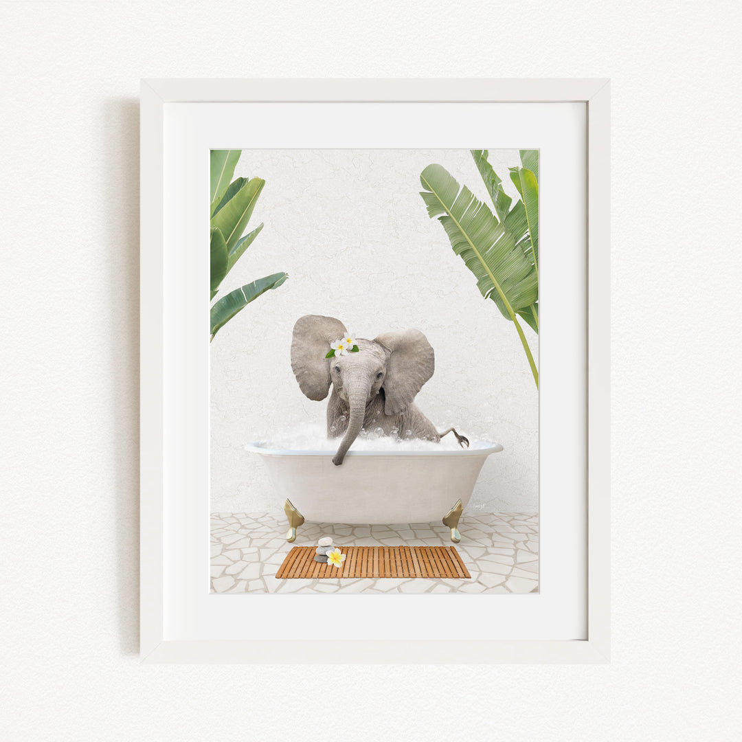 A gray elephant is sitting in a white bathtub filled with water, surrounded by green leaves and a wooden mat on the floor.