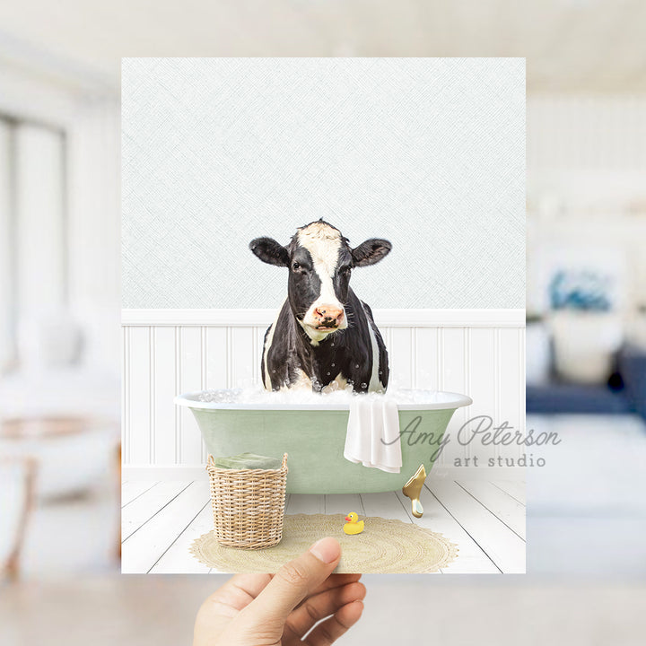 a hand holding up a picture of a cow in a bathtub