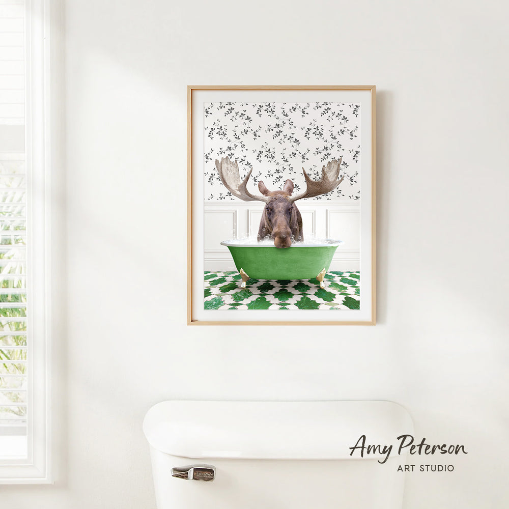 A framed image of a moose sitting in a green bathtub, with a patterned wall behind it.