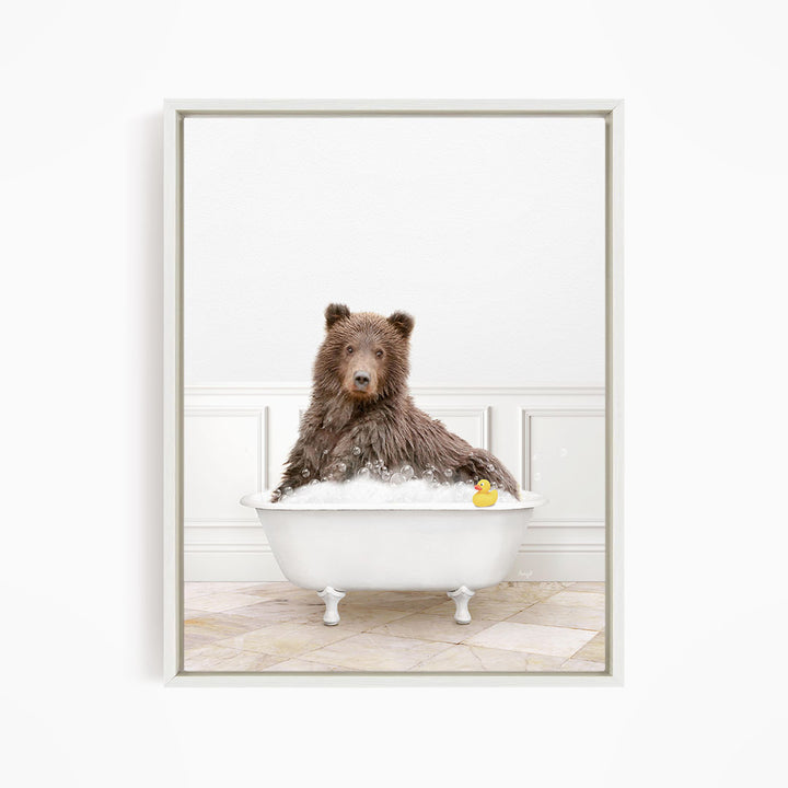 A brown bear sitting in a white bathtub filled with bubbles, with a rubber duck floating in the water.