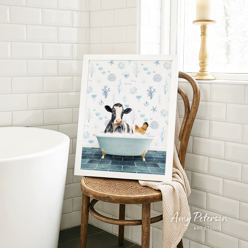 A framed painting depicting a cow and a chicken relaxing in a bathtub, surrounded by blue and white floral patterns.