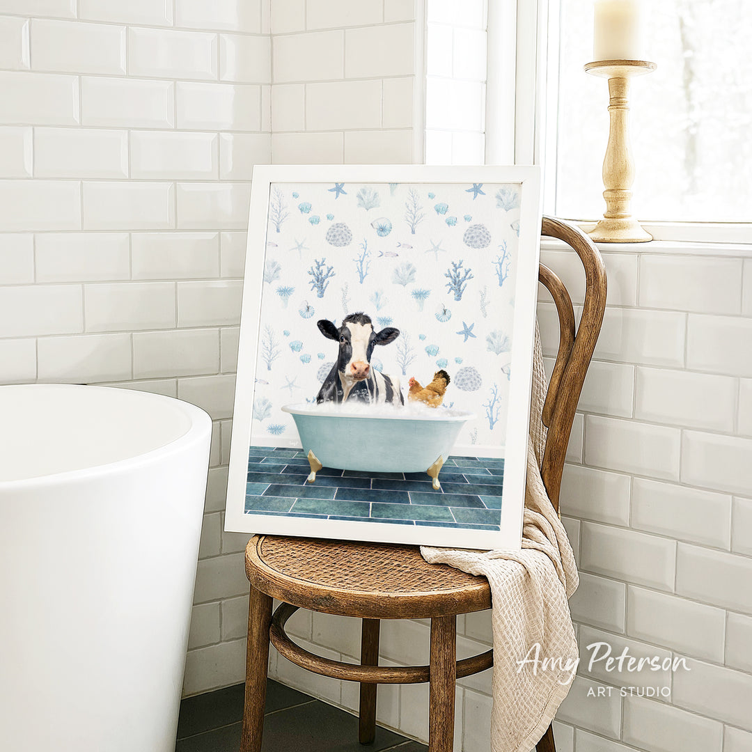 A framed painting depicting a cow and a chicken relaxing in a bathtub, surrounded by blue and white floral patterns.
