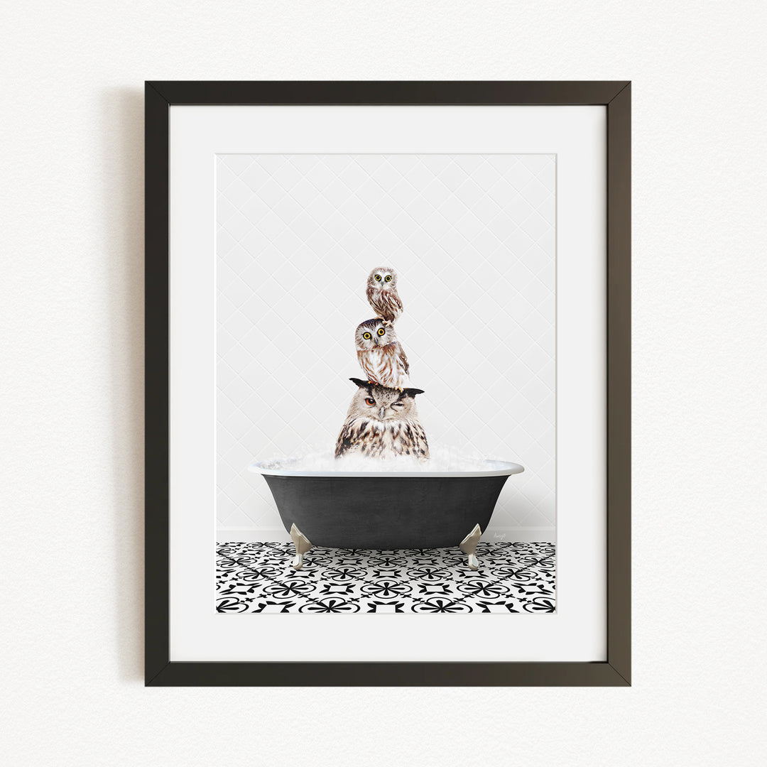 A framed image depicting a group of owls sitting in a bathtub, with one owl perched on top of the others.