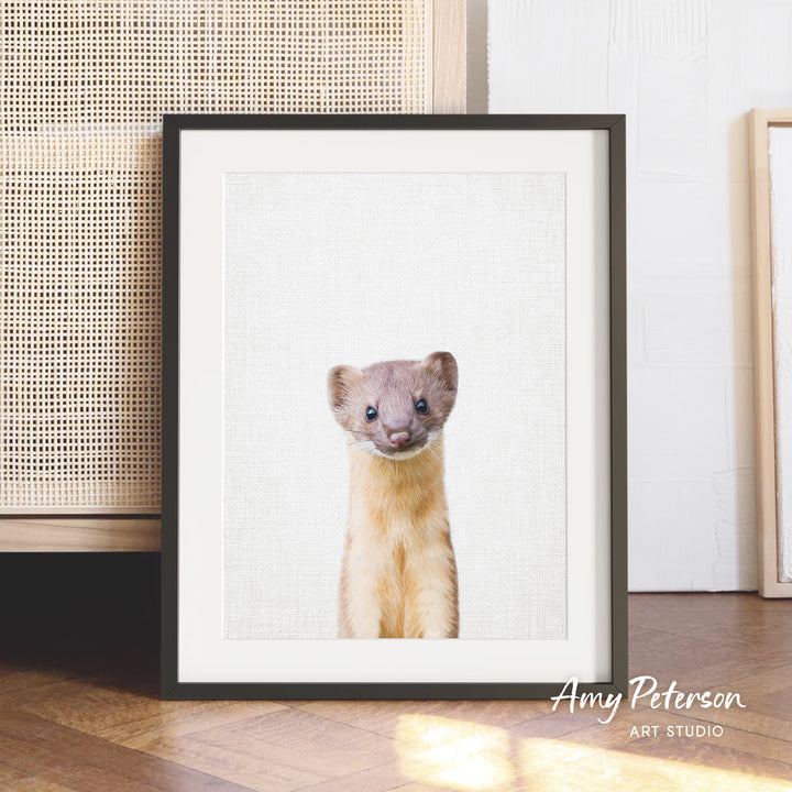 A framed photograph of a curious-looking animal, possibly a small rodent or rodent, is displayed on a wooden floor in front of a woven basket.