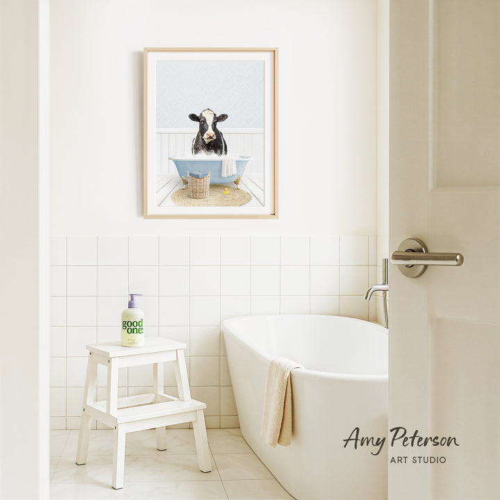 a bathroom with a white bathtub, a stool, and a framed picture of a cow sitting in a bathtub.