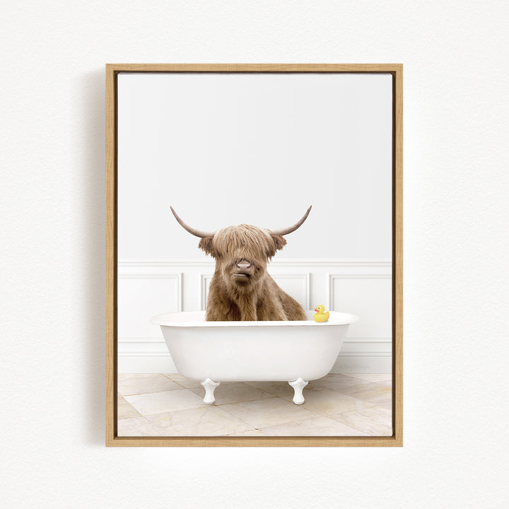 A brown cow with long horns is sitting in a white bathtub, with a yellow rubber duck floating in the water.