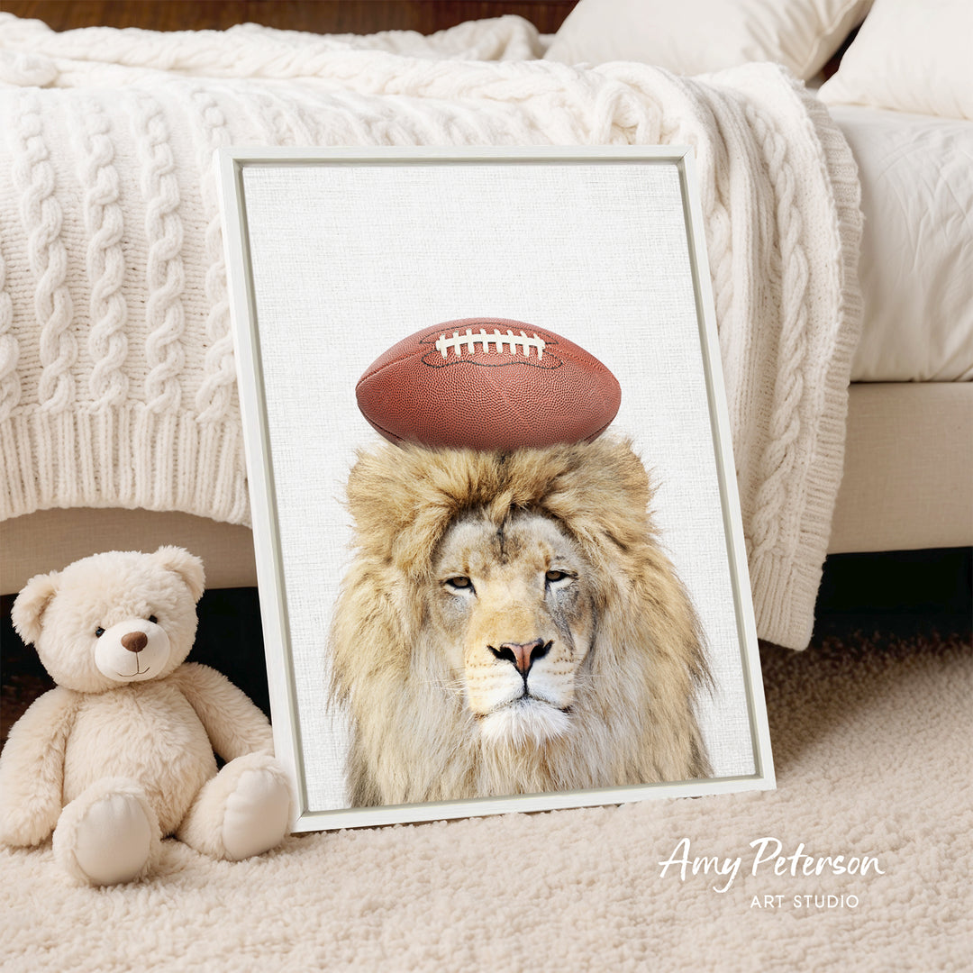 A framed print of a lion with a football on its head is displayed on a bed, accompanied by a teddy bear.