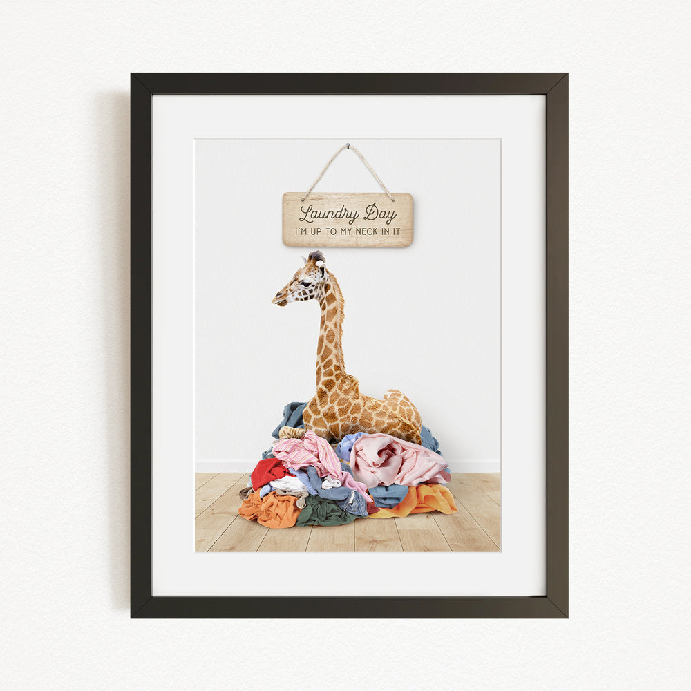 A giraffe sitting on a pile of clothes, with a sign above that says "Laundry Day".