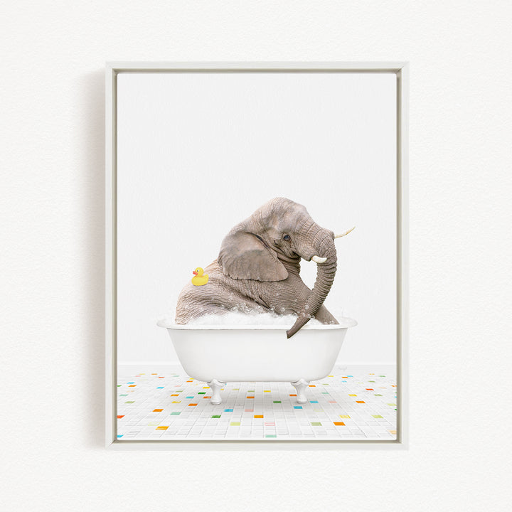 A gray elephant is sitting in a white bathtub, with a yellow rubber duck floating next to it.