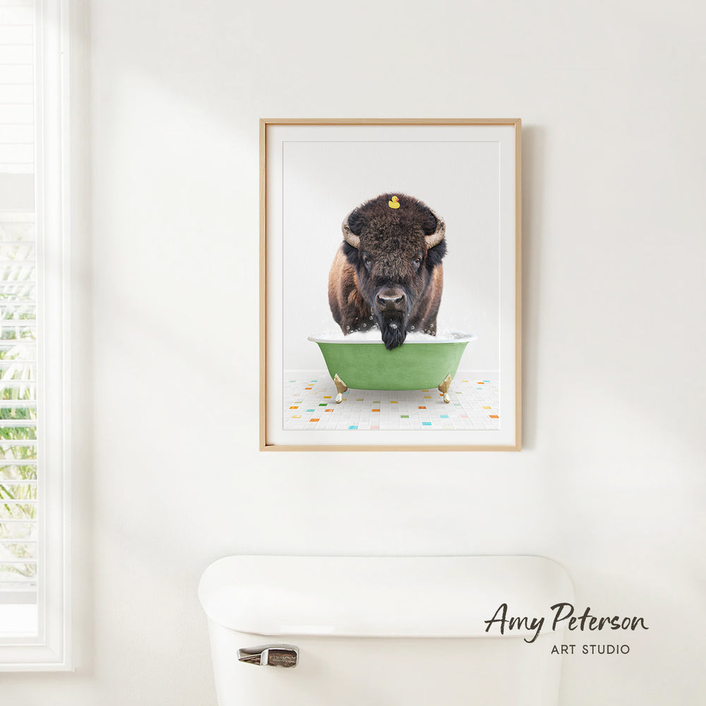 A framed image of a buffalo standing in a green bathtub, with a white toilet in the foreground.