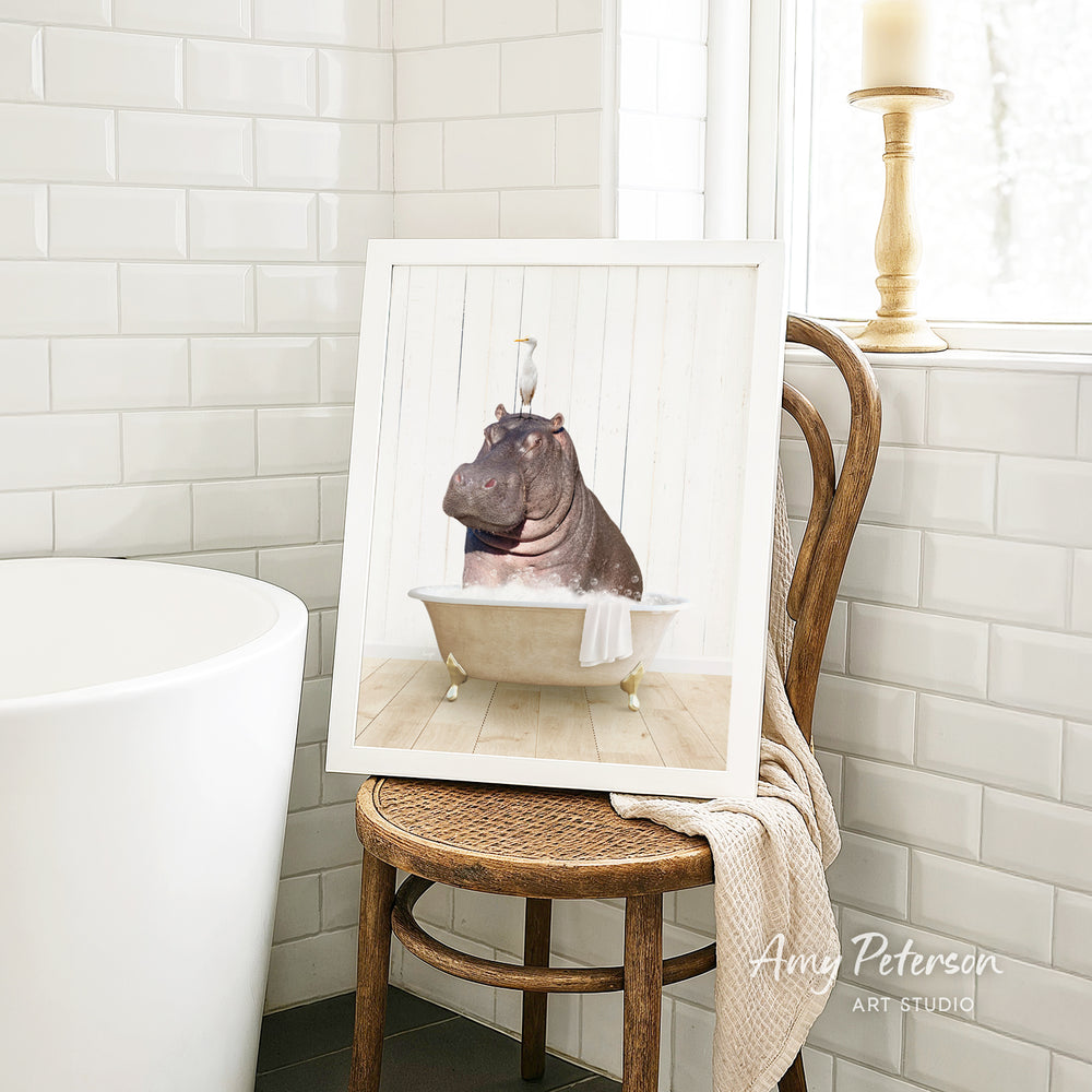A framed image of a hippopotamus sitting in a bathtub is displayed on a wooden chair in a bathroom setting.