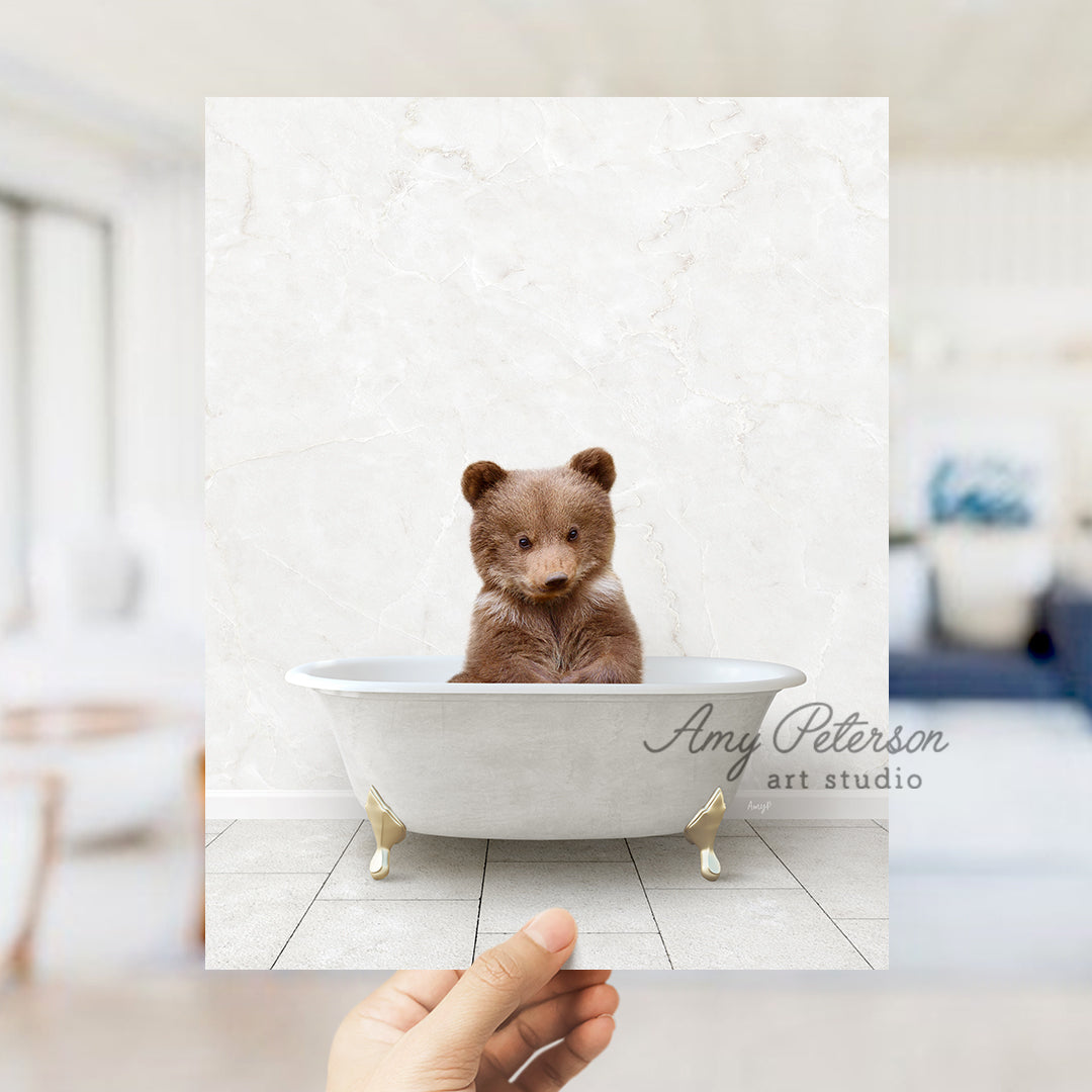 a hand holding a polaroid photo of a brown bear in a bathtub