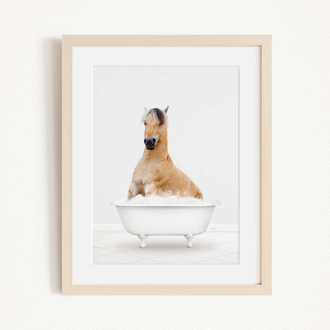 A light brown horse is sitting in a white bathtub filled with bubbles, looking directly at the camera.