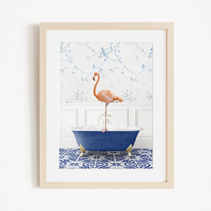 A framed image depicting a pink flamingo standing on the edge of a blue bathtub filled with water, set against a floral wallpaper background.