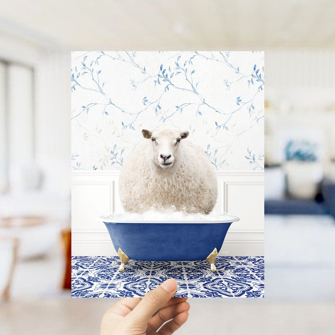 A fluffy white sheep sits in a blue bathtub, surrounded by a blue and white patterned floor and a white wall with blue floral wallpaper.