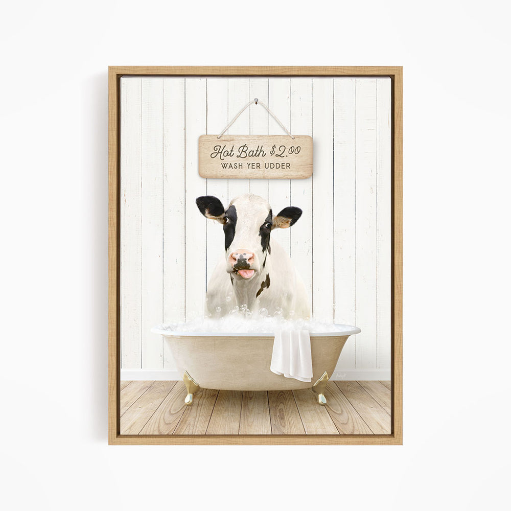 A black and white cow is sitting in a white bathtub, with a wooden sign above it that reads "Hot Bath $2.00 WASH YER UDER".