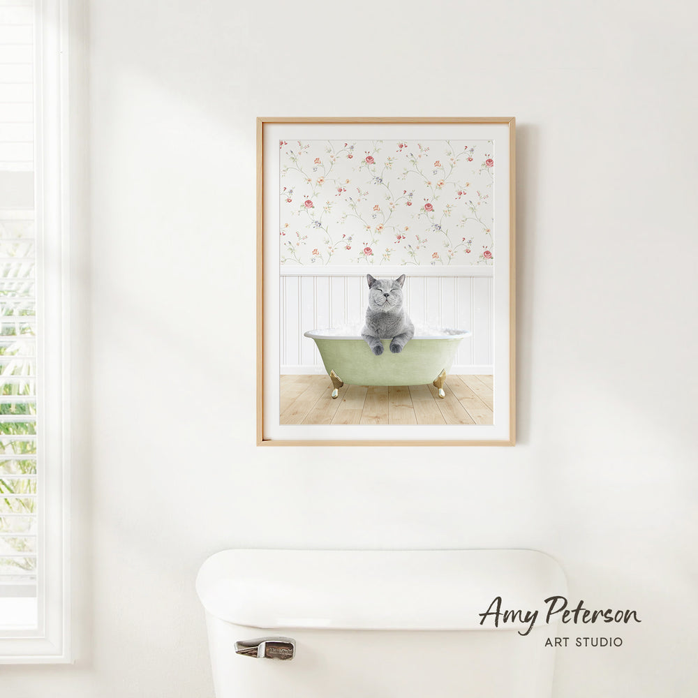 A framed image of a gray cat sitting in a green bathtub, with a floral pattern on the wall behind it.