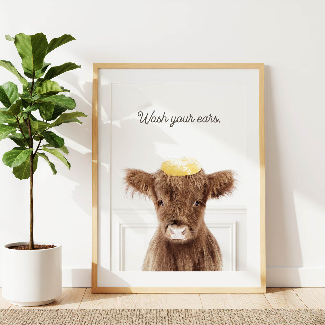 a framed picture of a brown cow with a yellow hat on its head, accompanied by the text "Wash your ears."