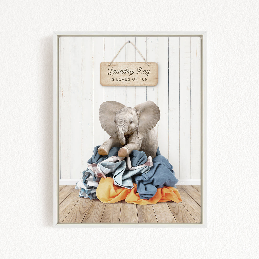 A framed image of a stuffed elephant sitting atop a pile of laundry, with a sign above that reads "Laundry Day is loads of fun".
