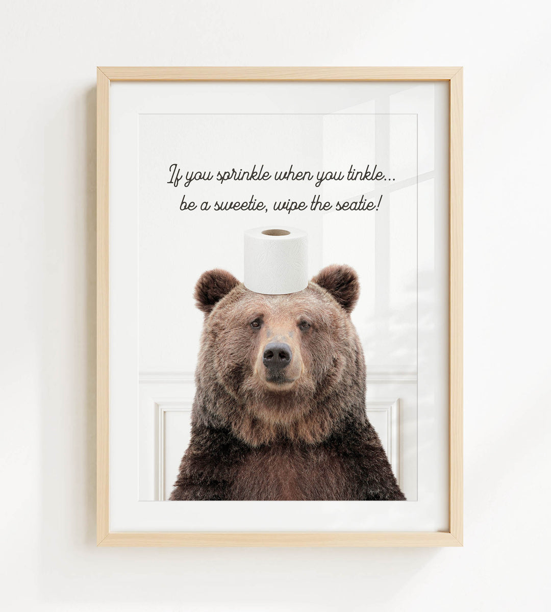 A framed image of a brown bear sitting on a roll of toilet paper, with the text "If you sprinkle when you tinkle... be a sweetie, wipe the seattle!" written above it.