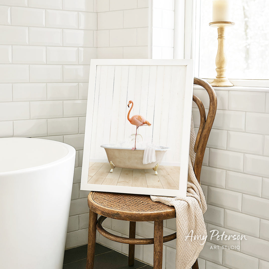 A framed image of a pink flamingo sitting in a bathtub is displayed on a wooden chair in a bathroom setting.