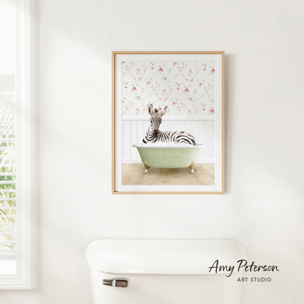 A framed print of a zebra sitting in a green bathtub is hanging on a white wall in a bathroom.
