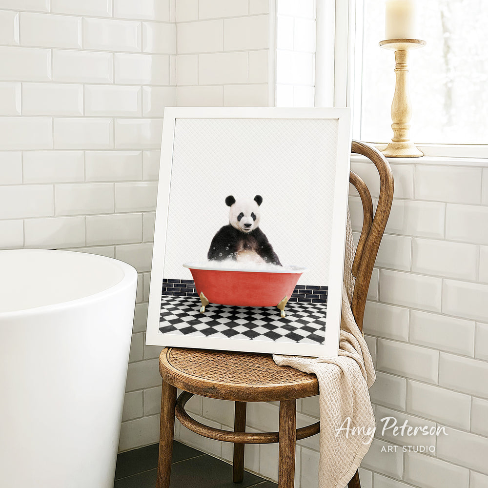 A framed image of a panda bear sitting in a red bathtub, surrounded by a black and white checkered floor, is displayed on a wooden chair in a bathroom setting.