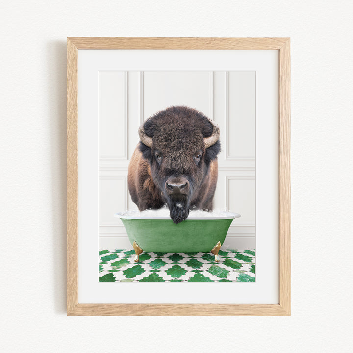 A buffalo with a black nose and brown fur is standing in a green bathtub filled with water, with a green and white patterned rug on the floor.