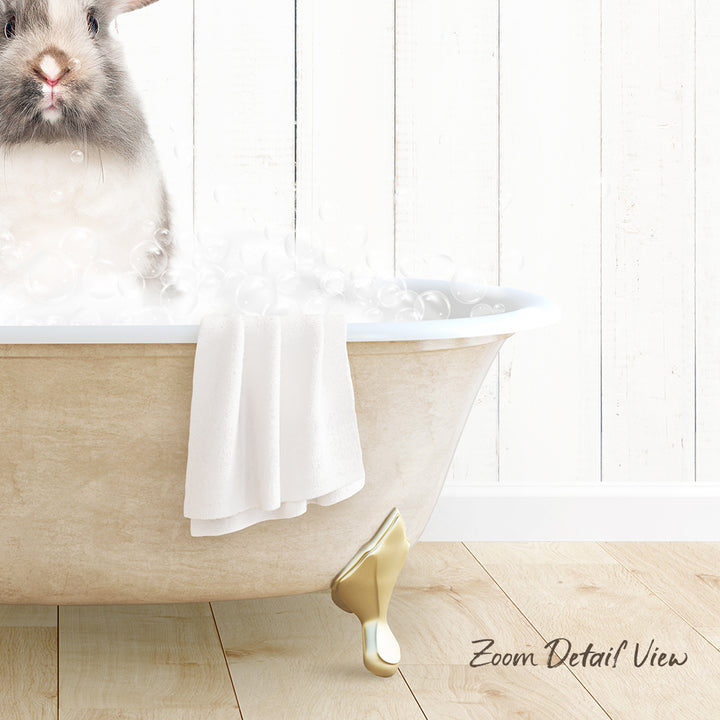A fluffy gray rabbit sitting in a white bathtub filled with bubbles, with a towel and gold bathtub leg visible.
