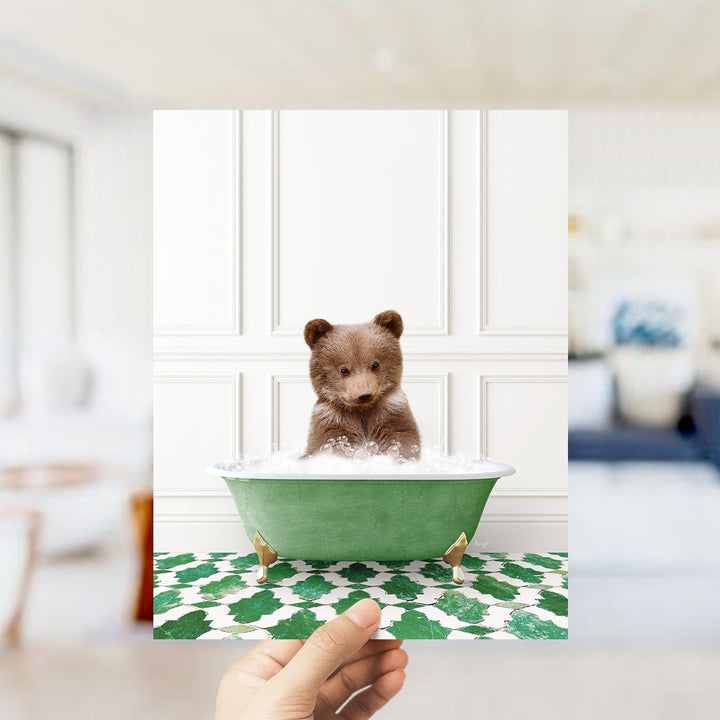 A small brown bear sitting in a green bathtub filled with bubbles, surrounded by a patterned green and white floor.