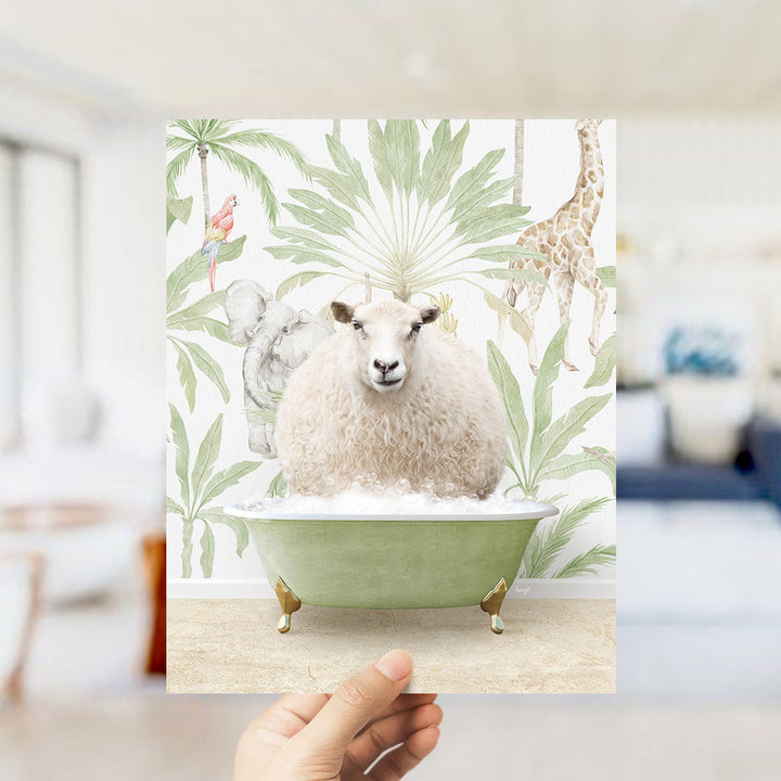 A hand holds up a framed print featuring a sheep sitting in a bathtub surrounded by tropical plants and animals, including a giraffe and a parrot.