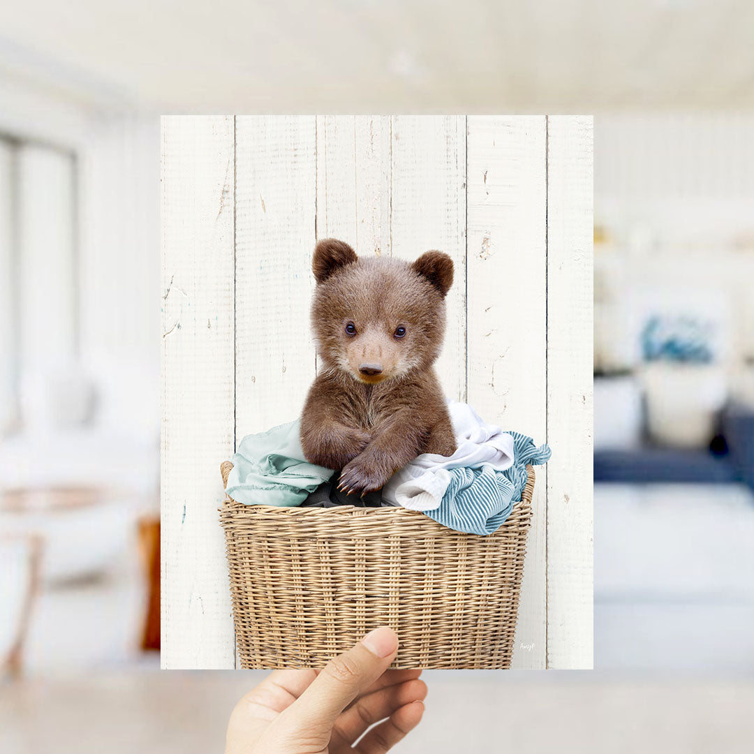A small brown bear sitting in a wicker basket filled with clothes.